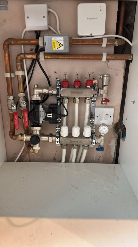 A neat, professional installation of an underfloor heating system, combining plumbing, electrical, and control elements.